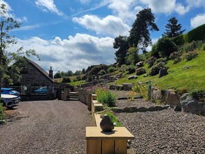 Un edificio de piedra con un camino de grava que lleva a un banco de madera con una decoración de piedra.