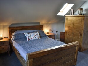 Un dormitorio con una cama de madera, una mesita de noche, una lámpara, un armario y un tragaluz.