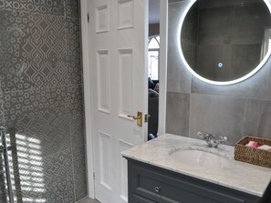 A bathroom with patterned tiles, a white door, a marble sink, and a round mirror. - 3 bedroom accommodation in Rothbury (Rothbury)