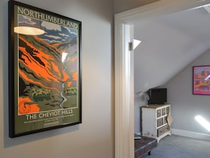 Un mapa enmarcado de las Colinas Cheviot en Northumberland, un dormitorio con un aparador blanco y un televisor sobre un soporte.
