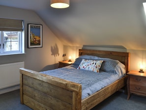 A bedroom with a wooden bed, a nightstand with a lamp, a window with a view, and a poster on the wall. - 3 bedroom accommodation in Rothbury (Rothbury)