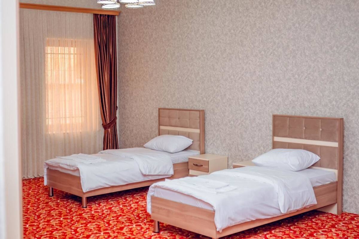 A hotel room with two single beds, a wooden headboard, a bedside table, and a red patterned carpet.