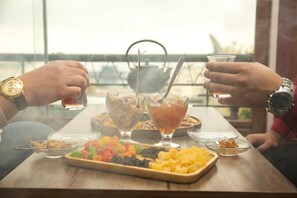 A table with various snacks and drinks, including a plate of colorful candies, a bowl of nuts, and two glasses of tea. - Soffia Hotel (Baku)