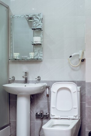 A bathroom with a pedestal sink, a toilet, a mirror with a decorative frame, and a hairdryer mounted on the wall. - Soffia Hotel (Baku)