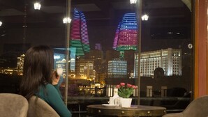 Una persona asseguda a la finestra amb vista a gratacels il·luminats de nit.