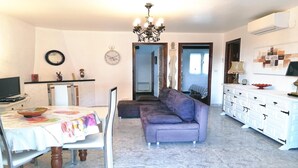 A living room with a sofa, a dining table with chairs, a TV, and a chandelier. - VACAY Villa Roger (L'ESCALA)