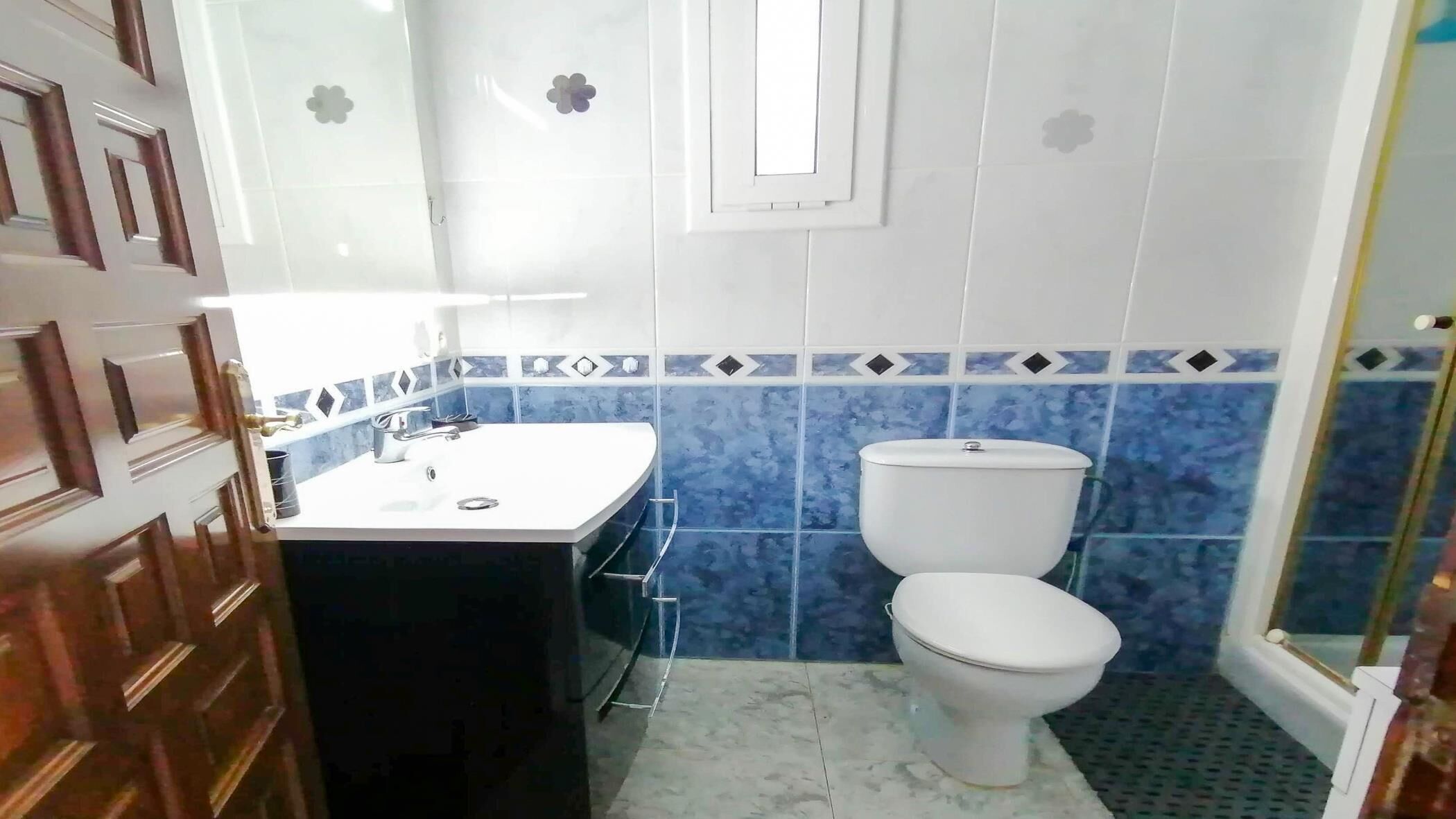 A bathroom with a white sink, a toilet, and blue patterned tiles.