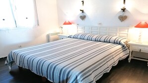 A neatly made bed with striped bedding, two bedside lamps, and heart-shaped wall decorations. - VACAY Villa Roger (L'ESCALA)