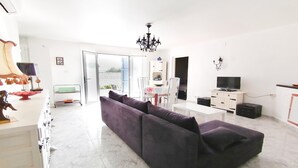 A modern living room with a dark-colored sofa, a white coffee table, a TV, and a chandelier. - VACAY Villa Roger (L'ESCALA)