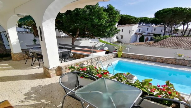 A pool area with a glass table and chairs, surrounded by stone walls and potted plants. - VACAY Villa Roger (L'ESCALA)