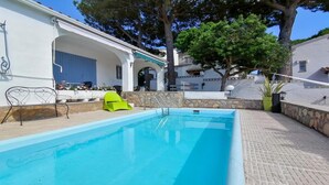 A swimming pool with a stone wall and a bright green chair. - VACAY Villa Roger (L'ESCALA)
