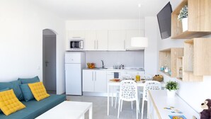 Un espacio habitable moderno y funcional, con kitchenette, comedor y sofá con cojines.