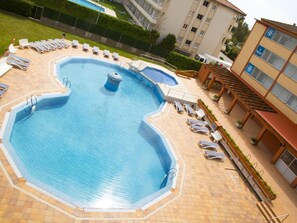 En swimmingpool med liggestole og en flisebelagt solterrasse.