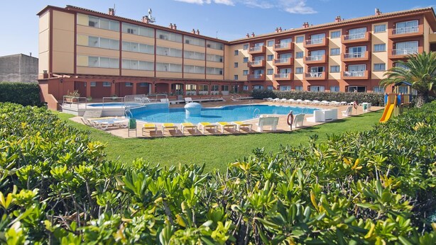 Un hotel con piscina, varios balcones y un césped bien cuidado.