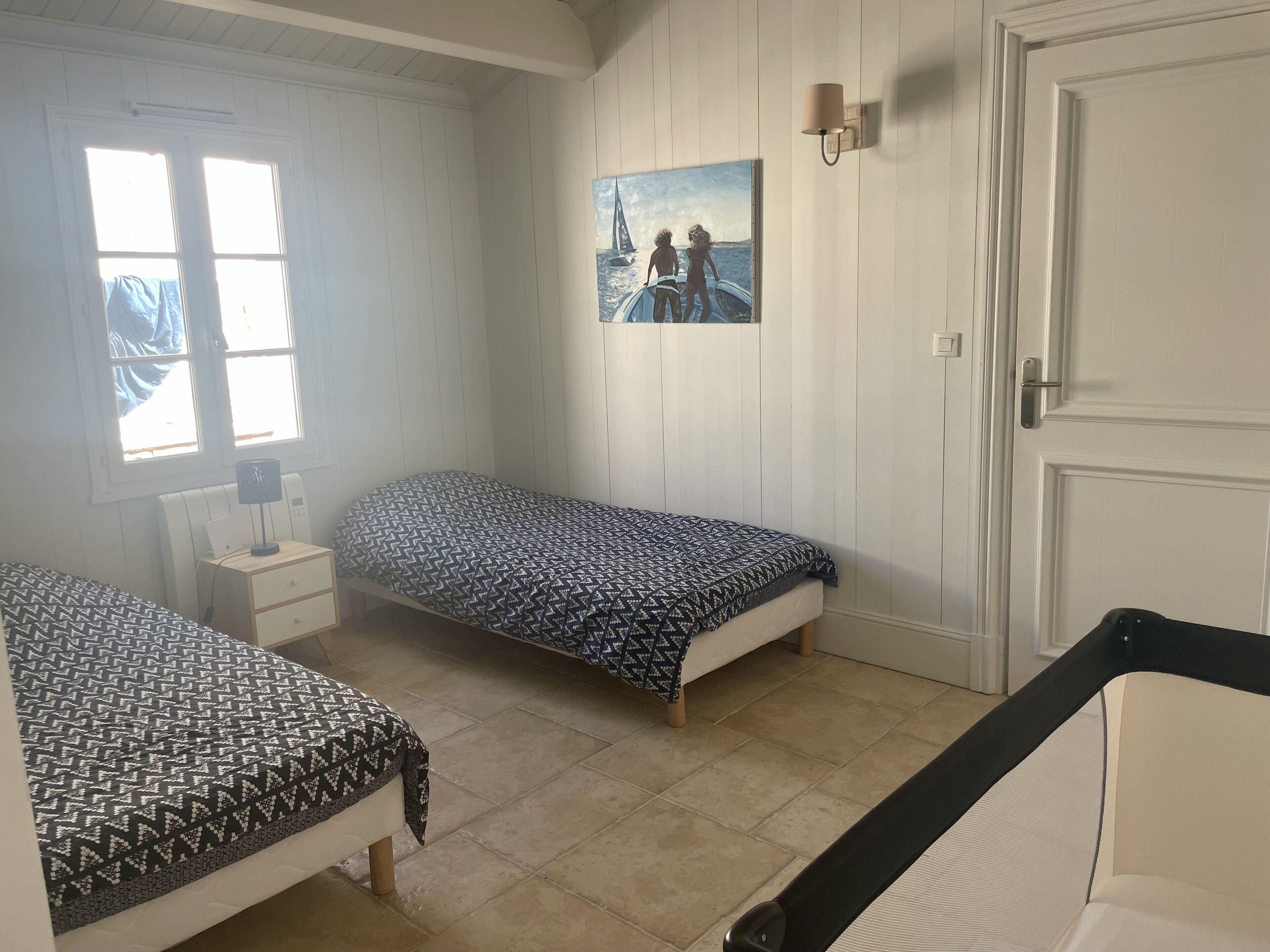 Una habitación con dos camas individuales, una mesita de noche con lámpara, un cuadro en la pared y una ventana con persianas.