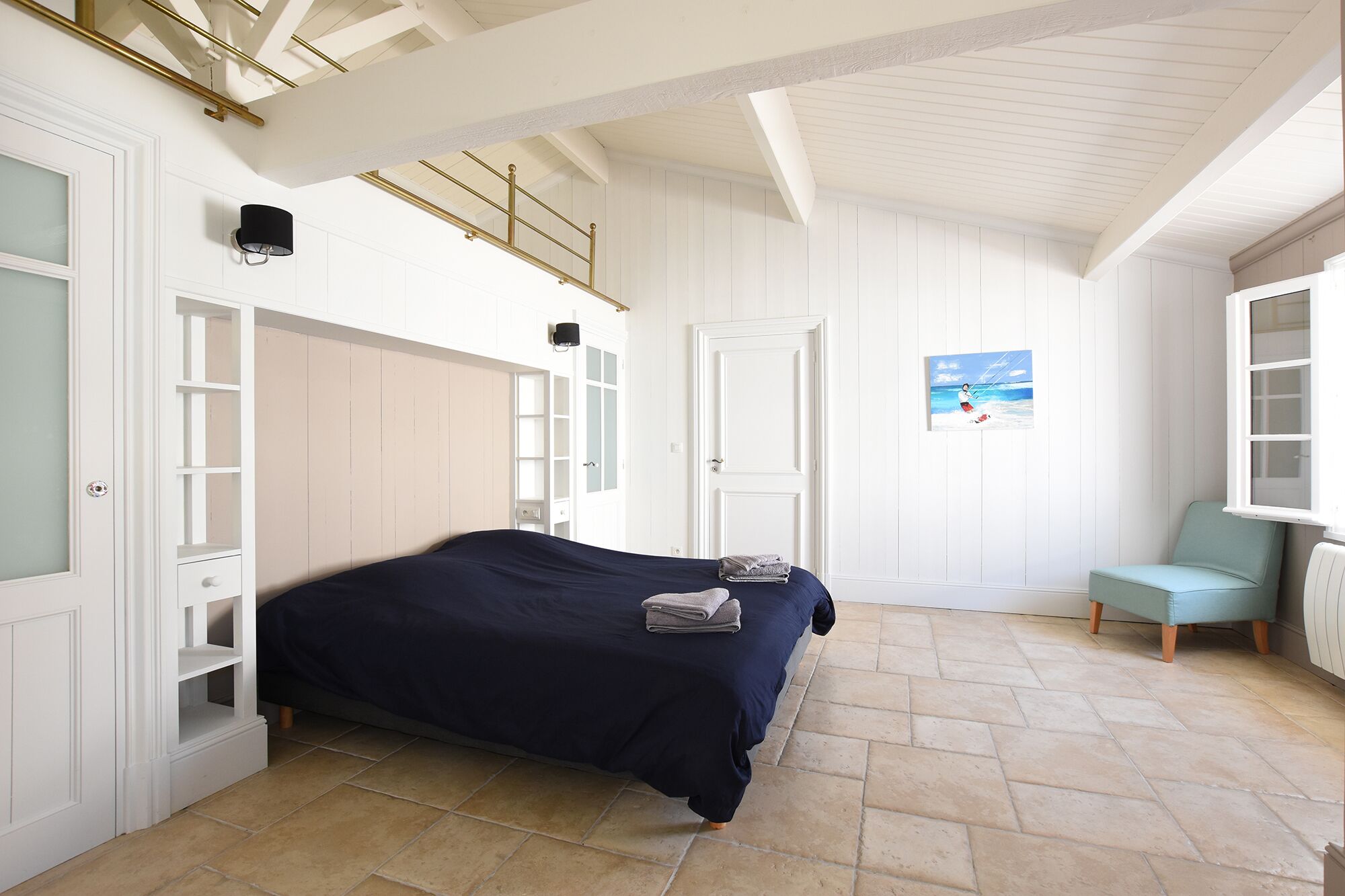 A bedroom with a bed, a chair, a painting, and a staircase.