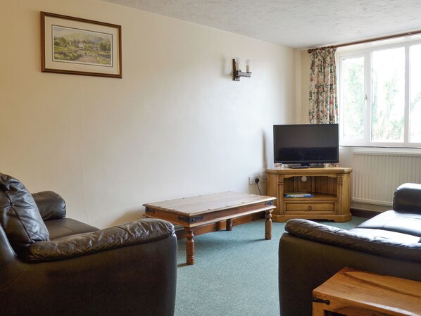 A living room with a television on a wooden stand, two leather sofas, a small wooden table, and a framed picture on the wall.