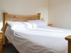 A single bed with a wooden headboard and two pillows, a bedside table with a lamp, and a nightstand with a drawer.