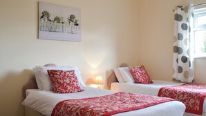 Une chambre d’hôtel avec deux lits, chacun étant doté de draps blancs et d’oreillers à motifs floraux rouges. Un tableau représentant des fleurs est accroché au mur, au-dessus des lits.