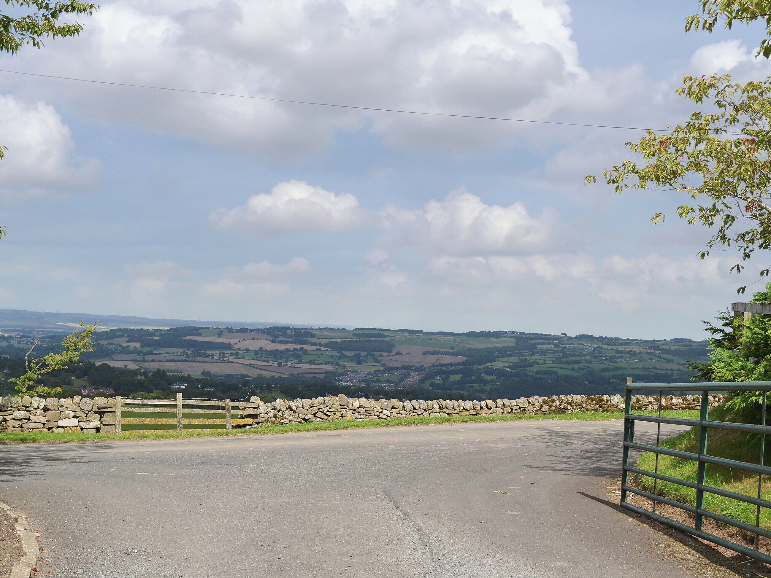 A rural road with a stone wall and wooden fence on one side, leading to a stone gate.