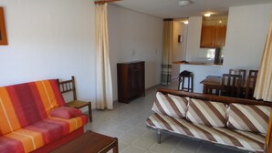 Una sala de estar con un sofá, una mesa de madera y una cocina al fondo.