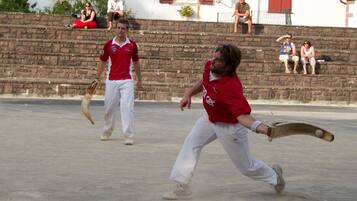 Partido de críquet en desarrollo, con jugadores uniformados de rojo y blanco en un campo de hormigón.