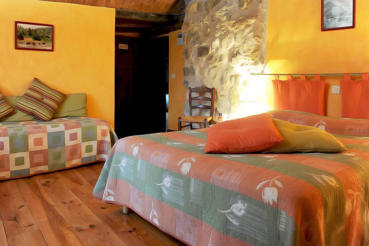 Une chambre avec deux lits, un plancher en bois, un mur en pierre et un tableau accroché au mur.