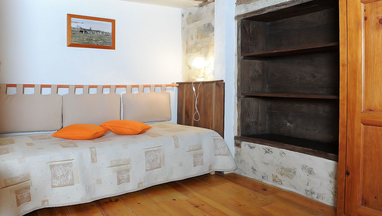 Ein Schlafzimmer mit einem Bett, einem Holzschrank, einer an der Wand befestigten Ablage und einem gerahmten Bild.