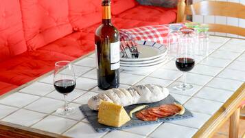 Une table dressée avec une bouteille de vin, des verres, des assiettes, un pain, du fromage et des tomates en tranches.