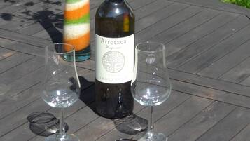 Una botella de vino Arretxea, dos copas y un par de gafas de sol sobre una mesa de madera al aire libre.