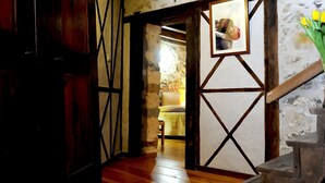A narrow hallway with wooden beams and a stone wall. A bed with a yellow blanket is visible in the background. - Chambres d'Hôtes Idiartekoborda (Saint-Etienne-de-Baigorry)