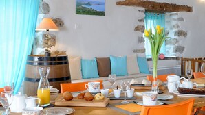 A breakfast setup with a wooden table, orange chairs, and a stone wall backdrop. - Chambres d'Hôtes Idiartekoborda (Saint-Etienne-de-Baigorry)