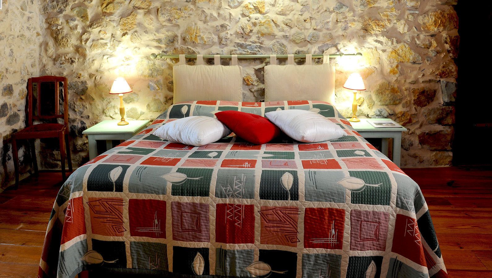 Una cama con colcha en una habitación con paredes de piedra y dos lámparas de noche.