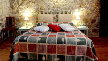 Una cama con colcha en una habitación con paredes de piedra y dos lámparas de noche.