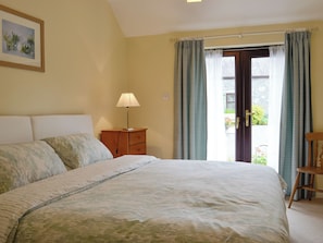 A bedroom with a bed, a nightstand, a lamp, and a door leading to an outdoor area.
