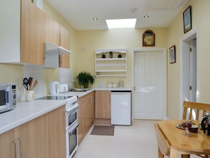 Cocina compacta con microondas, estufa, lavavajillas y pileta. Hay una mesa de comedor con sillas y un reloj en la pared.