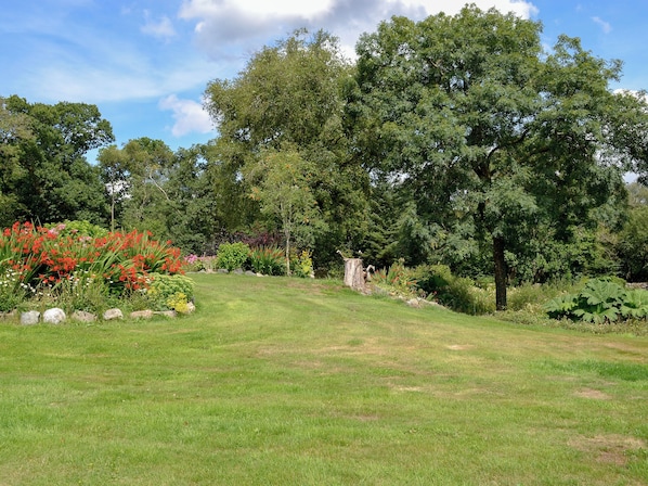 A well-maintained garden with a variety of plants and trees, a grassy lawn, and a stone pathway.