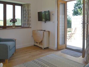 Een kamer met een bank, een televisie, een houten kast en een schuifdeur naar een buitenruimte met een stoel.