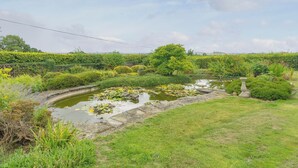 En fredfyldt have med en sø, frodig vegetation og en stensti.