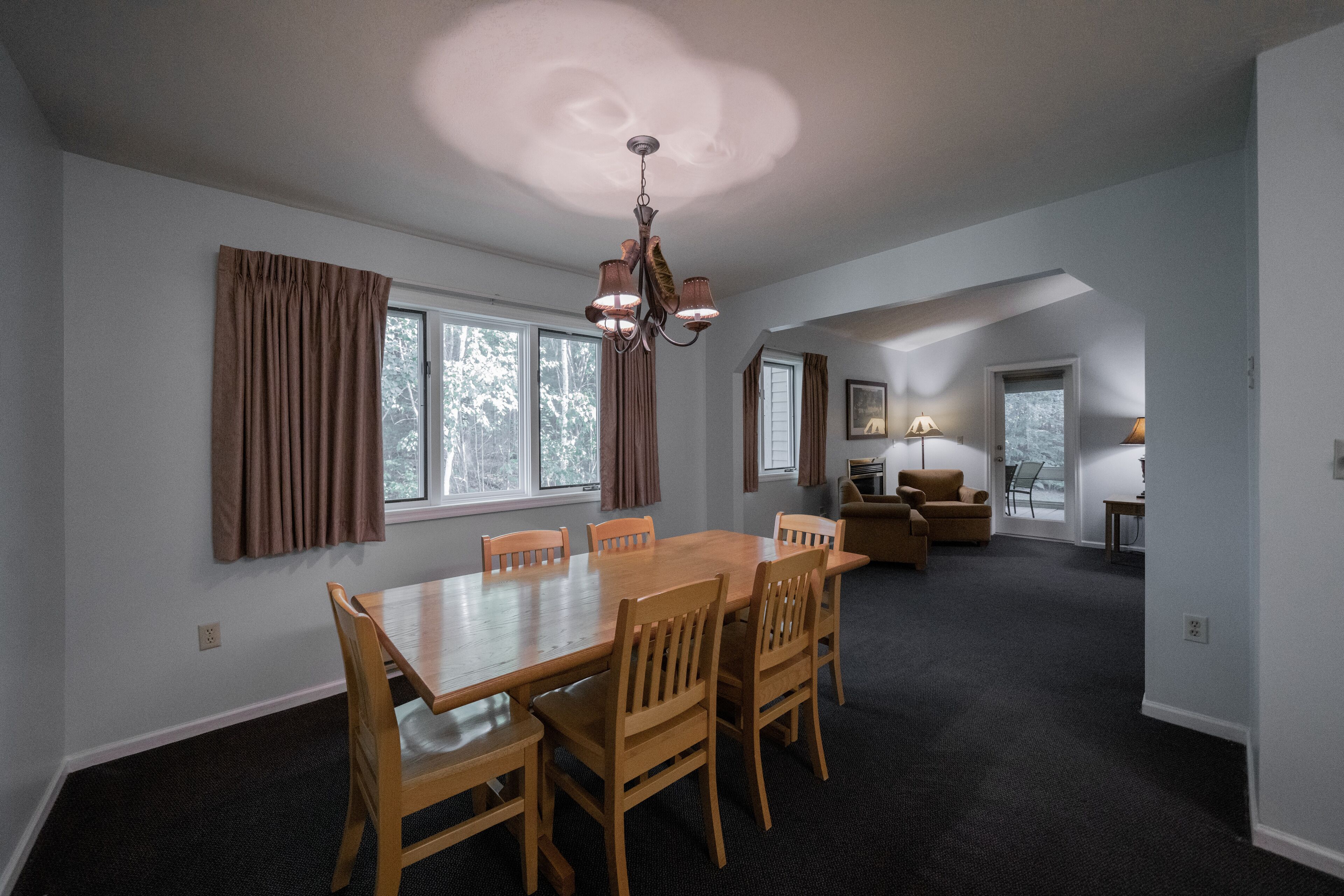 A spacious dining area with a wooden table and chairs, a chandelier, and large windows with curtains.
