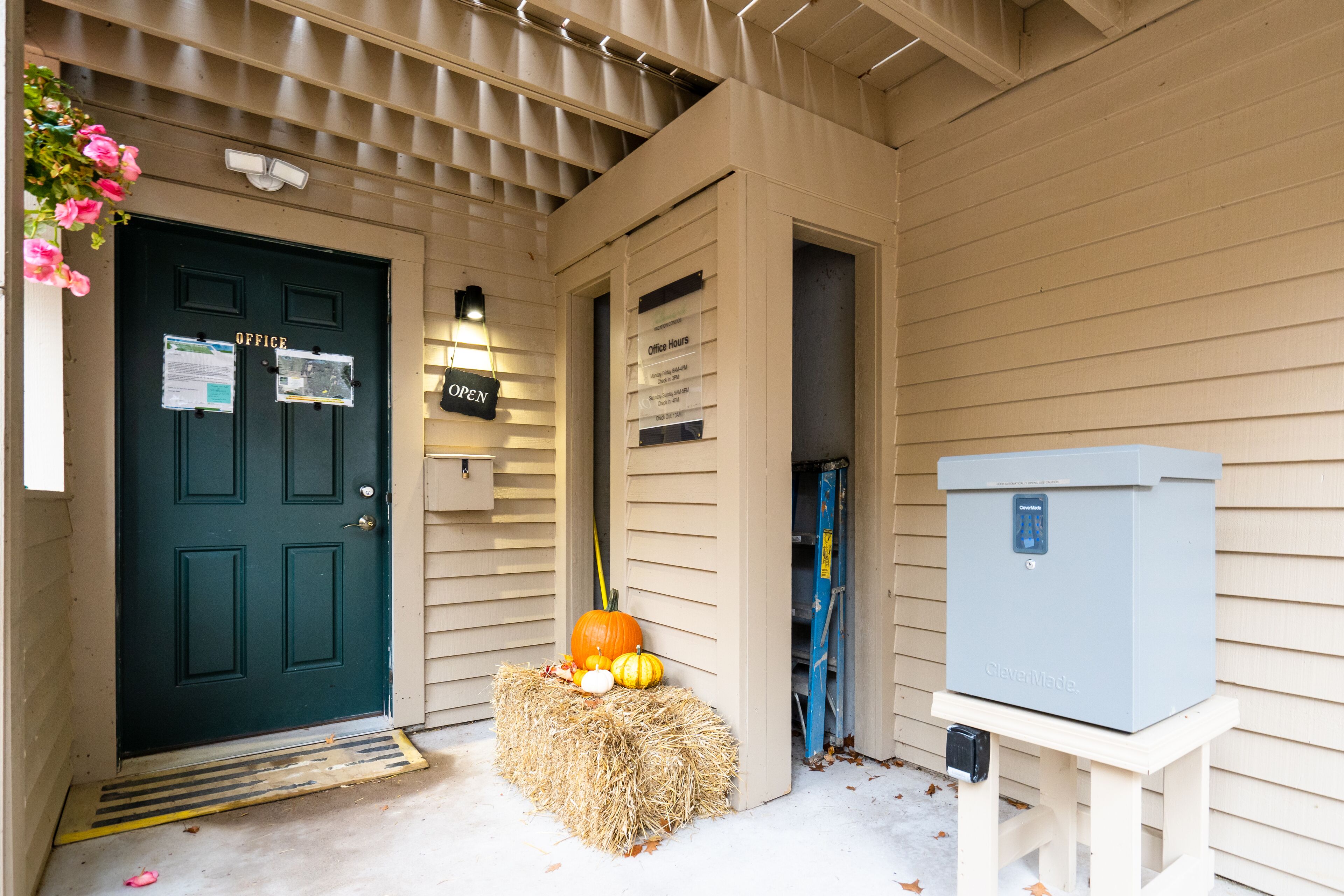 A front door with a sign indicating office hours, a hay bale decoration, and a utility box.