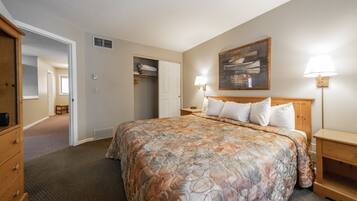A hotel room with a large bed, a wooden headboard, two bedside tables with lamps, a wardrobe, and a painting on the wall.