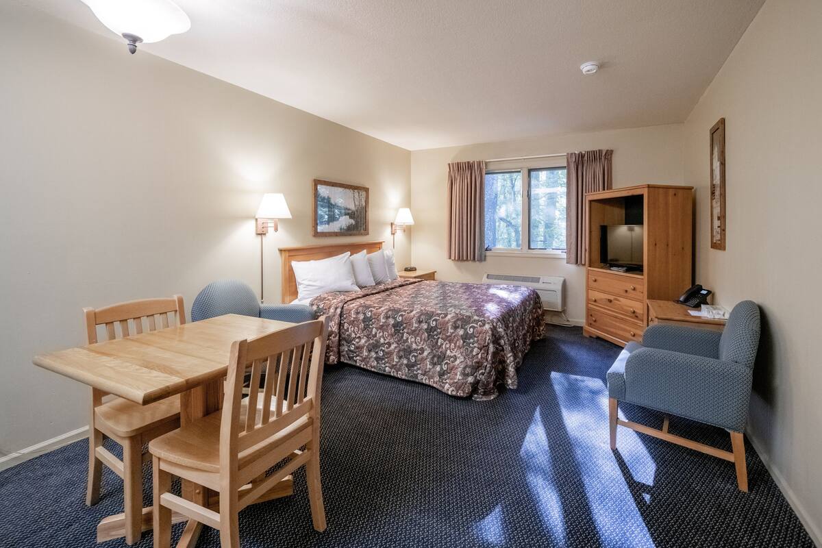 A hotel room with a wooden bed, a desk, a chair, a television, and a window with curtains.