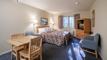 A hotel room with a wooden bed, a desk, a chair, a television, and a window with curtains.