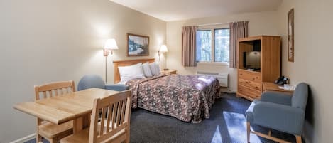 A hotel room with a wooden bed, a desk, a chair, a television, and a window with curtains.