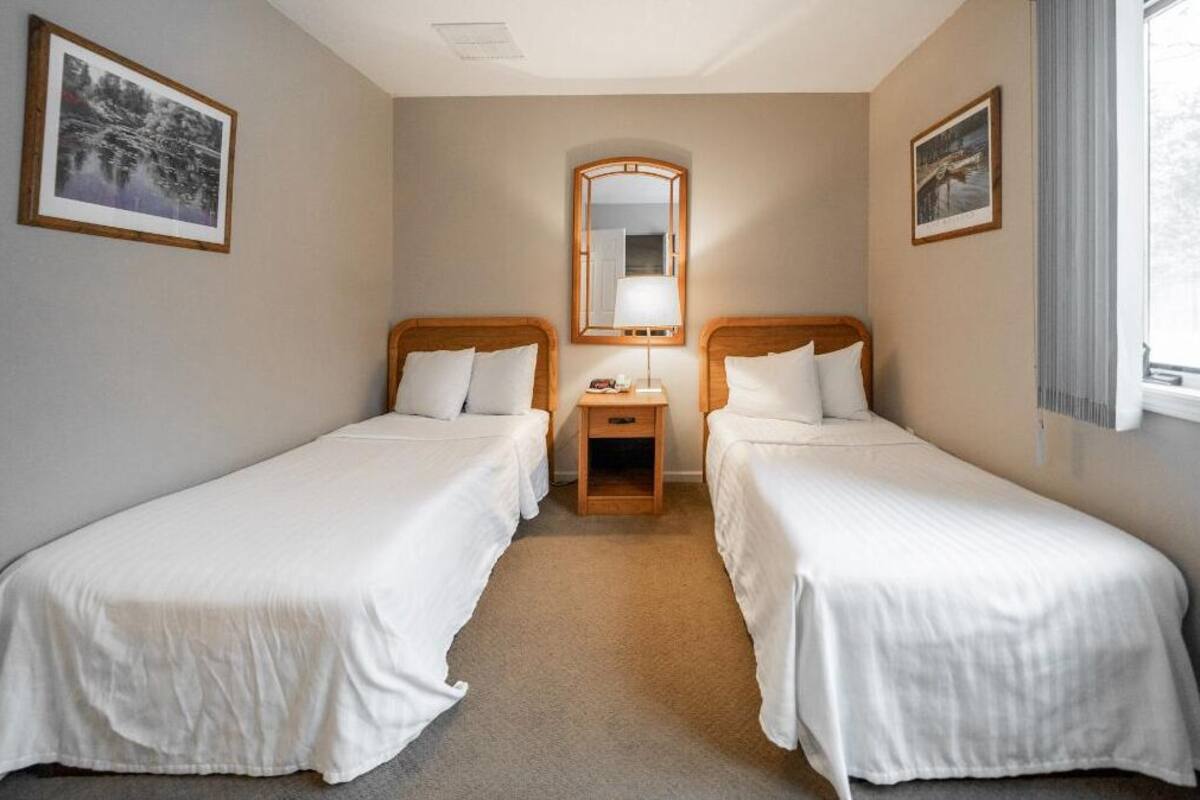 A hotel room with two single beds, a wooden nightstand, a mirror, and framed pictures on the walls.