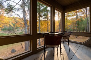 A wooden deck with two wicker chairs and a table, overlooking a forest with autumn foliage. - Telemark Northwoods Lodging (Cable)