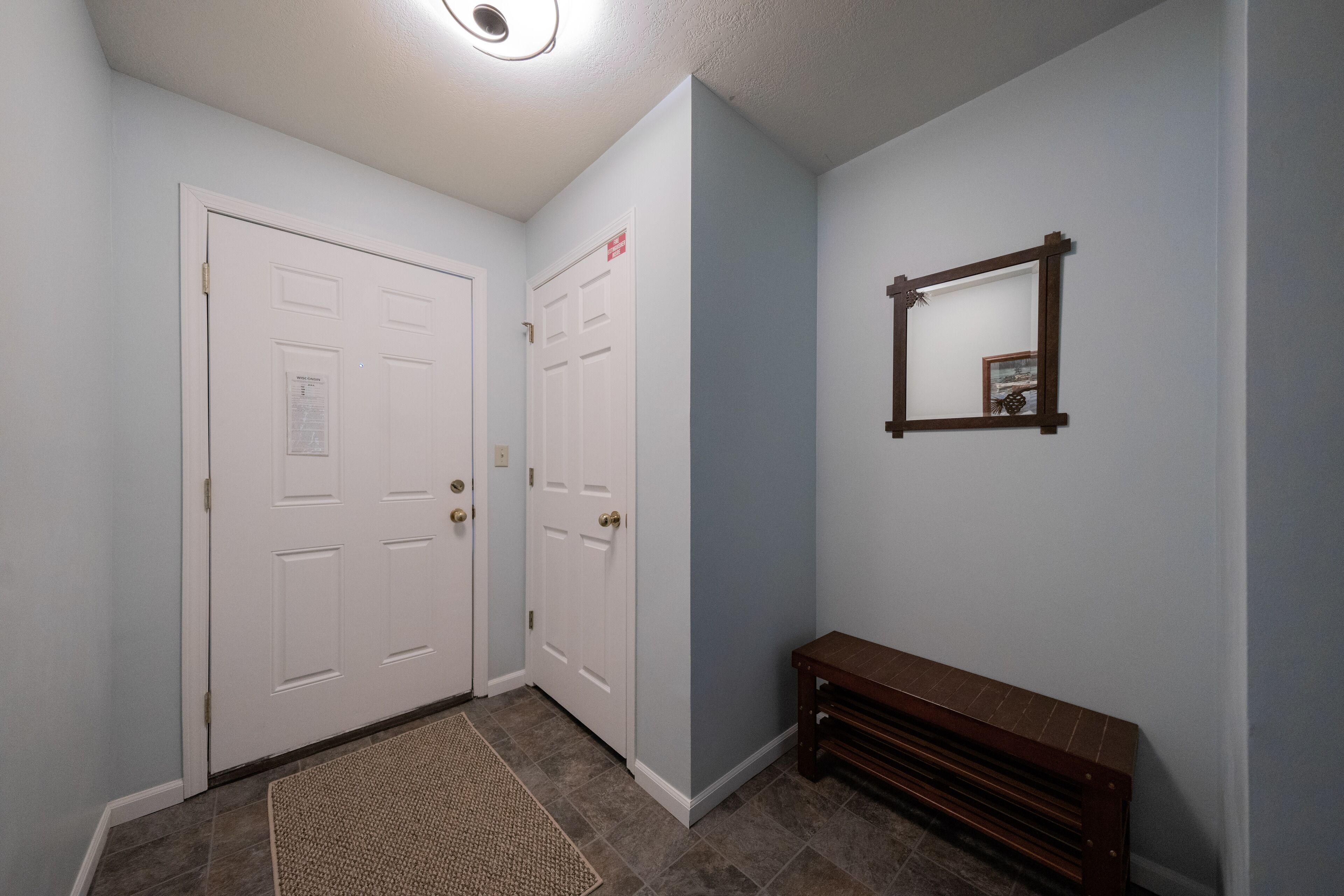Un couloir avec deux portes blanches, un banc en bois et un miroir accroché au mur.