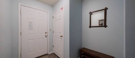 Un couloir avec deux portes blanches, un banc en bois et un miroir accroché au mur.