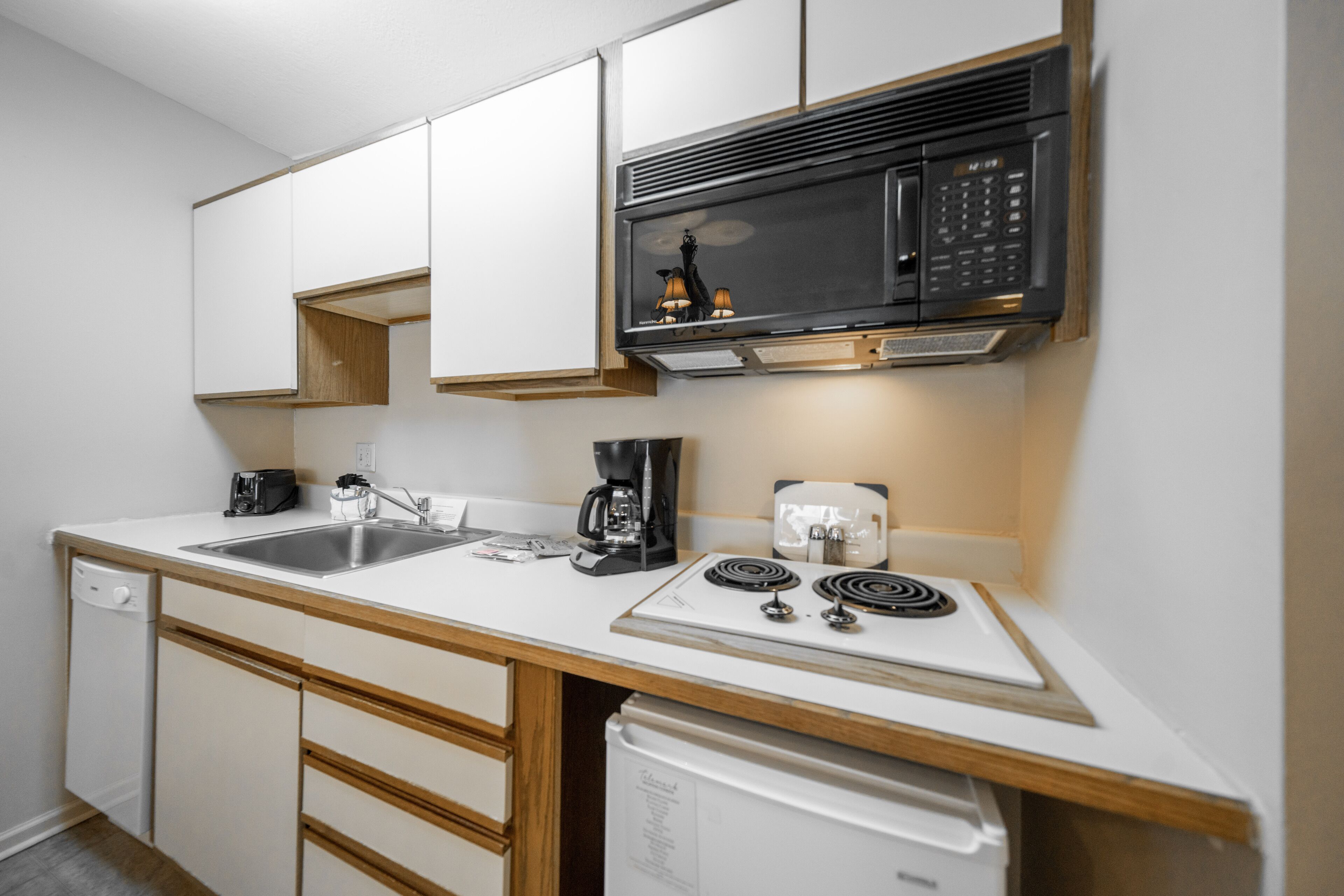 A compact kitchen with white cabinets, a microwave, a coffee maker, and a dishwasher.